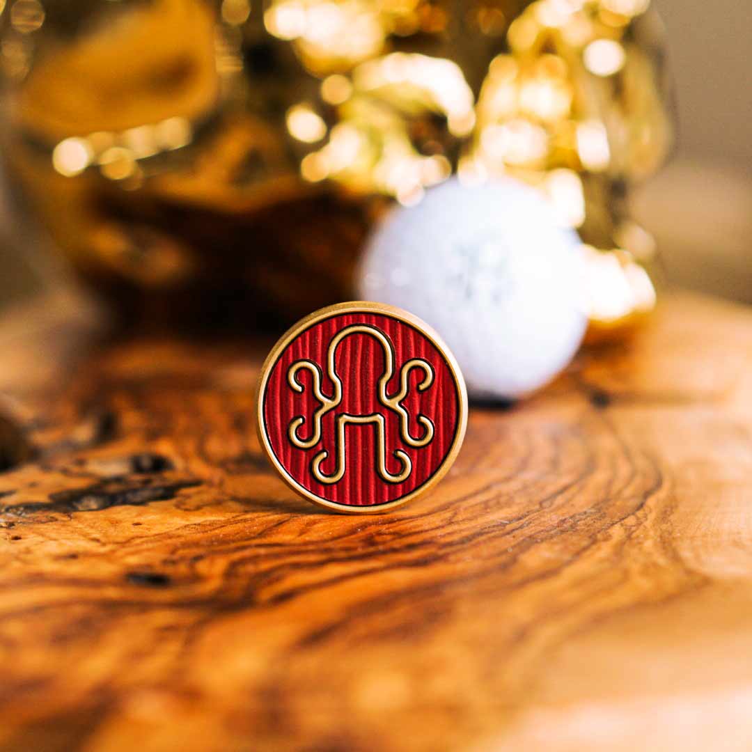 Brass golf ball marker with deep red leather inlay and engraved Kraken emblem, designed for bold golfers who disrupt tradition and mark with intent.