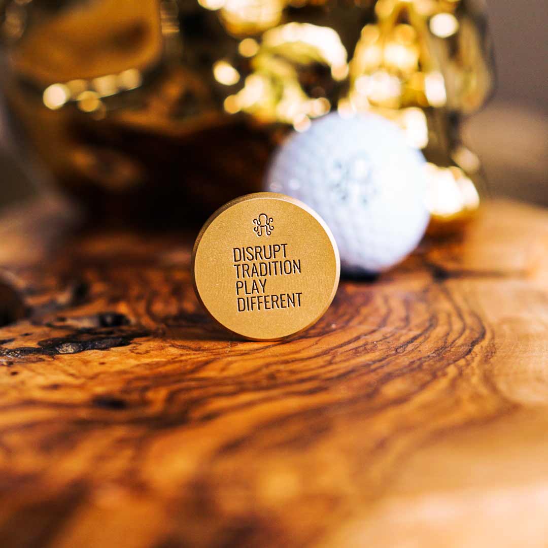 Brass golf ball marker with deep red leather inlay and engraved Kraken emblem, designed for bold golfers who disrupt tradition and mark with intent.