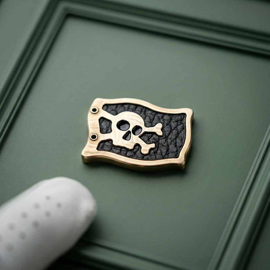 Brass pirate flag ball marker with black pebble grain leather inlay and raised skull