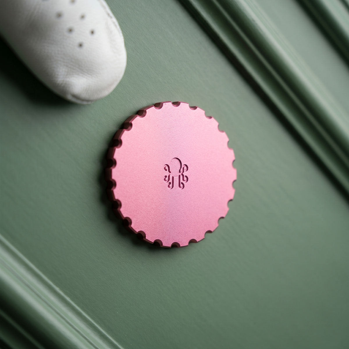Reverse of the pink anodized Last Laugh golf ball marker showing the engraved Kraken logo and gear-tooth edge
