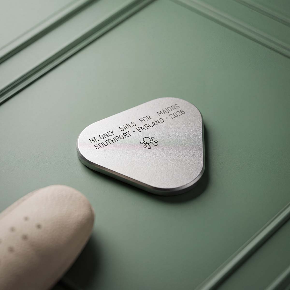 Reverse of the SHORE LEAVE ball marker, satin bead-blast stainless steel engraved HE ONLY SAILS FOR MAJORS, SOUTHPORT England 2026, with Kraken logo