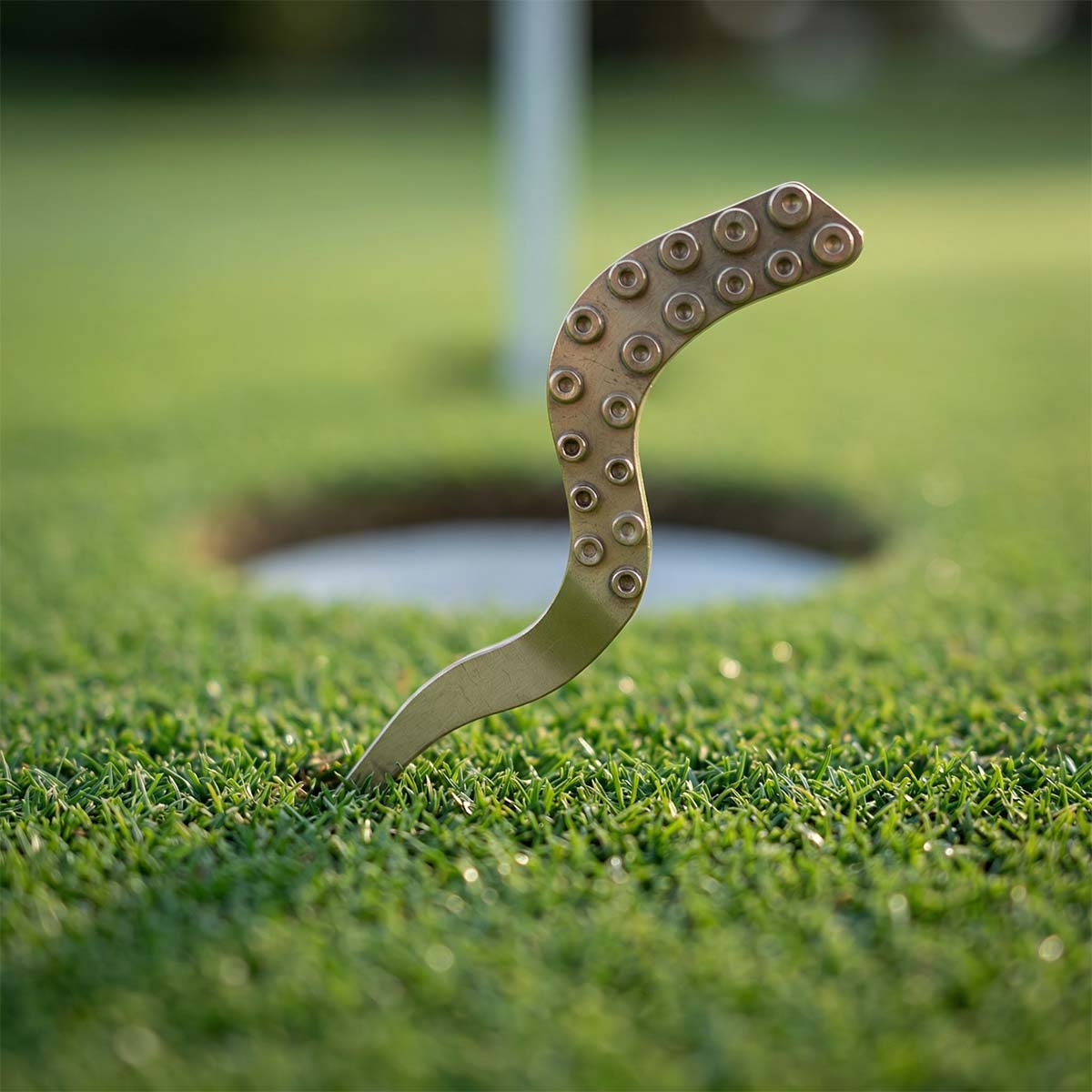 Kraken Golf Tentacle Pitch Tool in matte satin brass on putting green