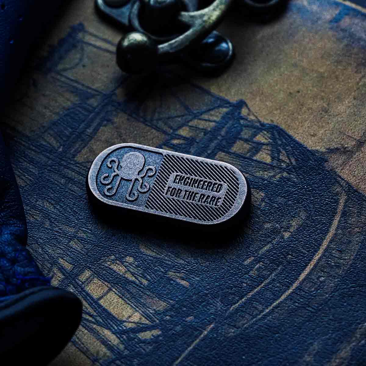 Darkened copper golf ball marker engraved with Kraken Golf logo and the phrase "Engineered for the Rare"