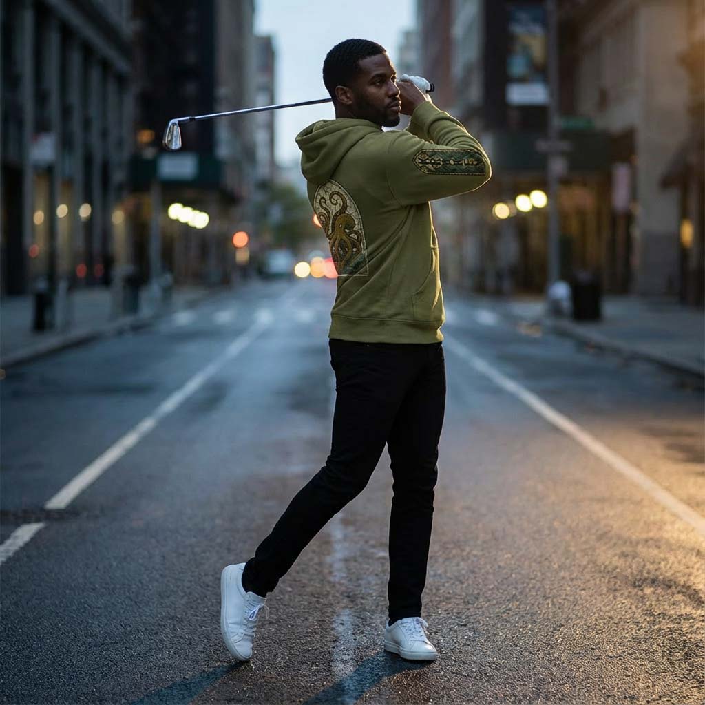 Golfer Jameel in the Acushnet Parish hoodie and black pants holding a golf club on an urban street.