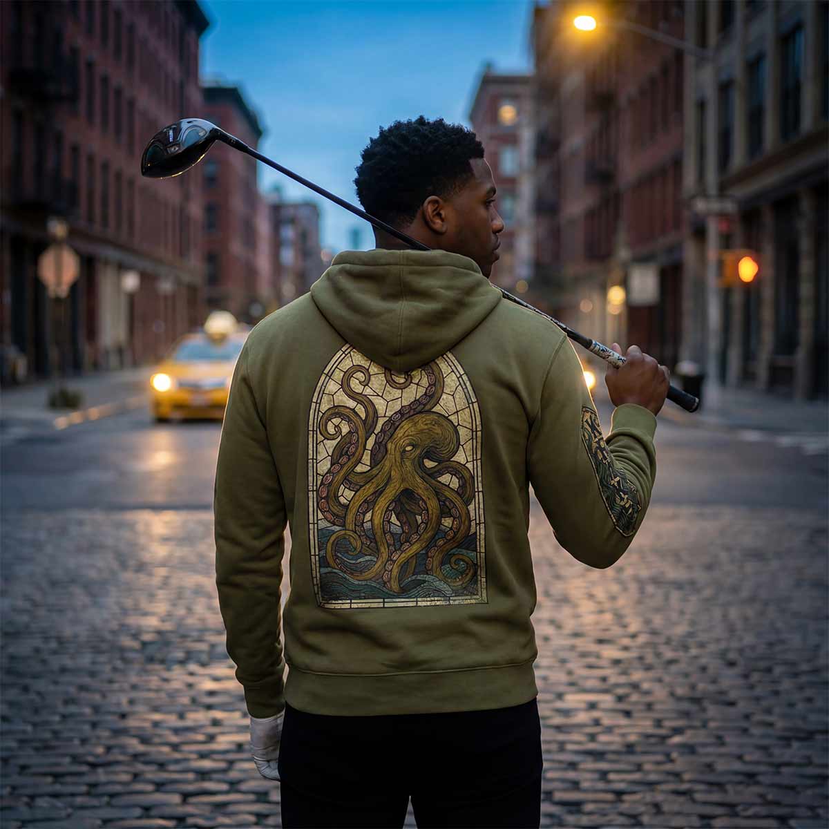 Person wearing the Kraken Golf Acushnet Parish hoodie with an octopus design on a city street at dusk