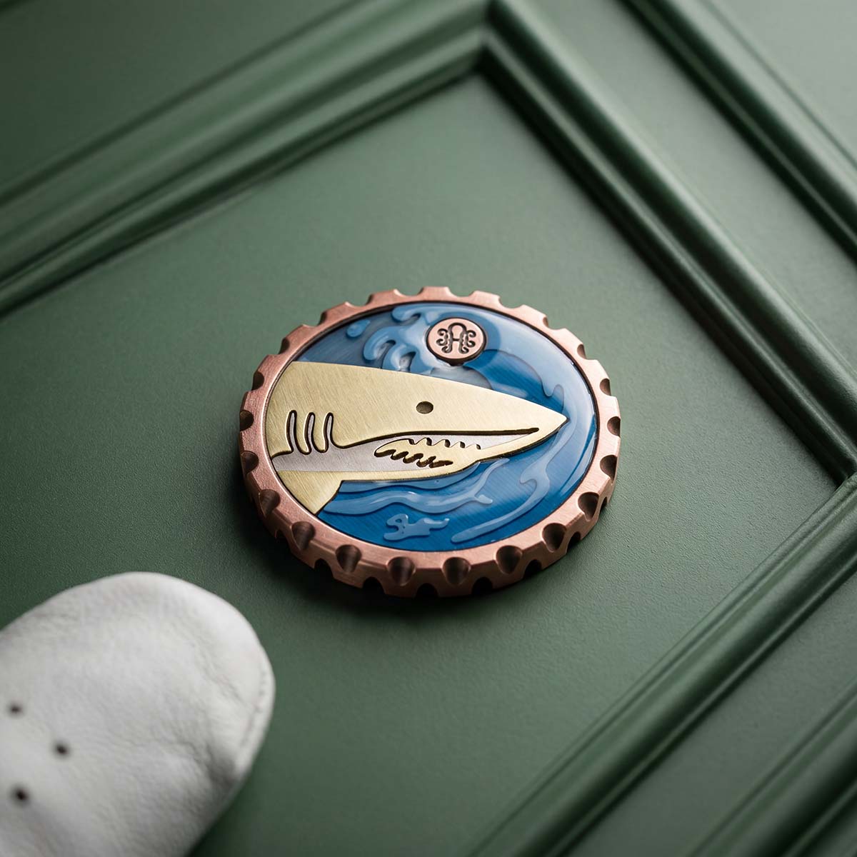 Brass and stainless steel shark inlay set into a sculpted resin ocean wave relief on the reverse of a solid copper Kraken Golf ball marker, with the Kraken mark in the upper corner.