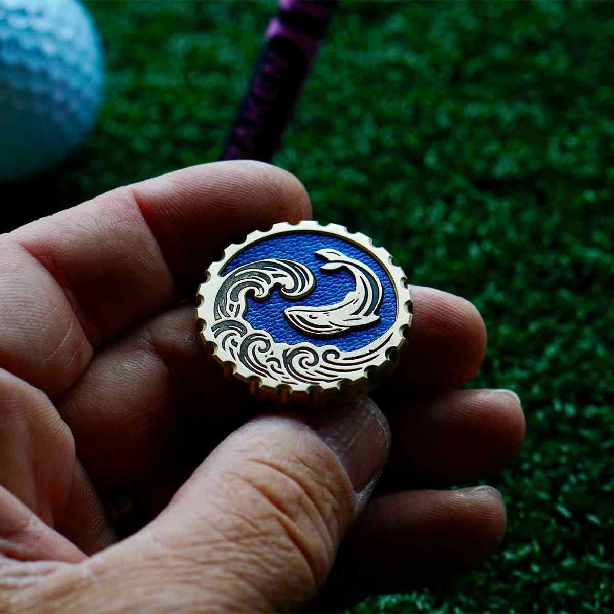 Beachfront Escape golf marker reverse side with engraved brass waves, embossed whale mid-flip, and sky blue leather background - Kraken Golf limited run