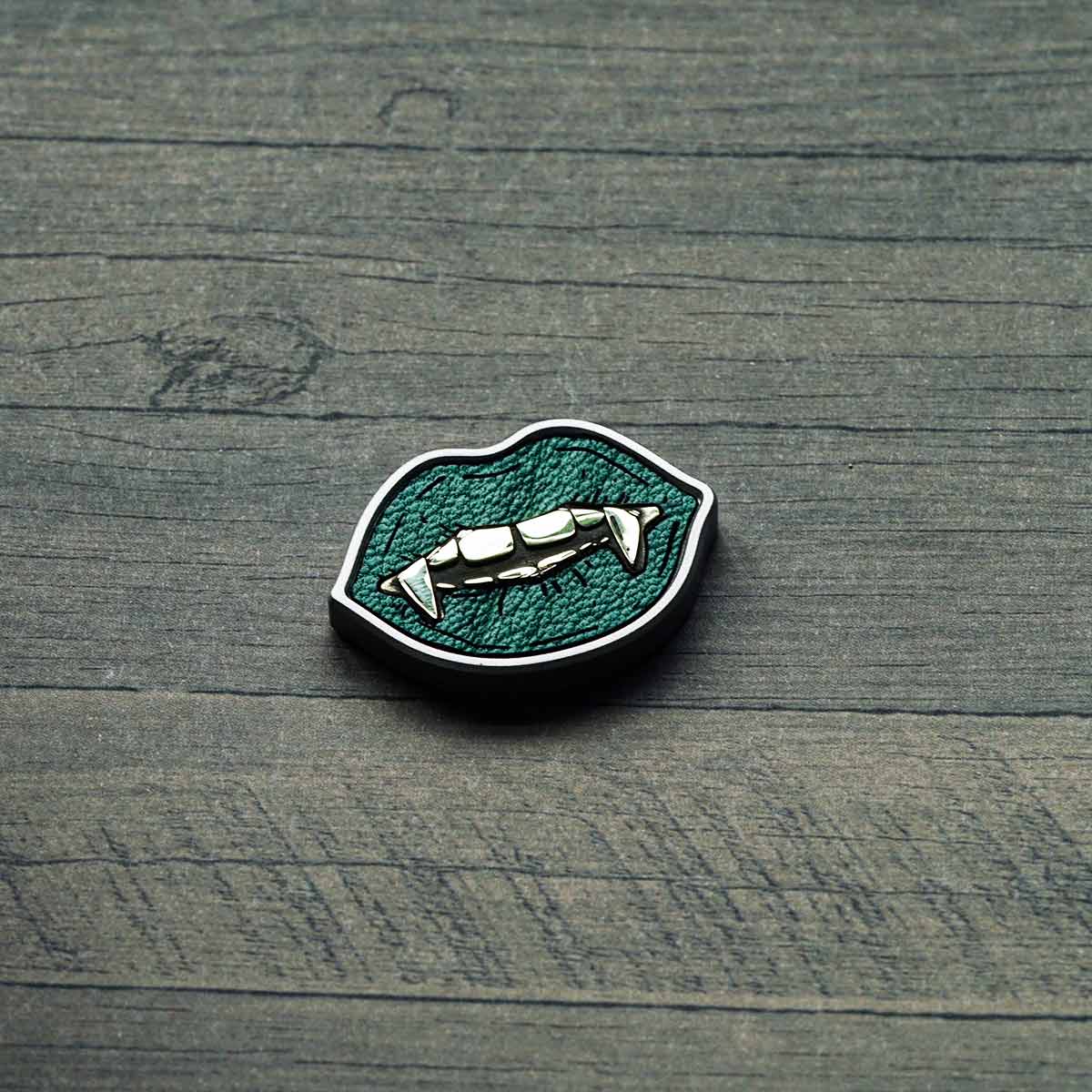 stainless steel golf ball marker with green leather inlay and brass fangs