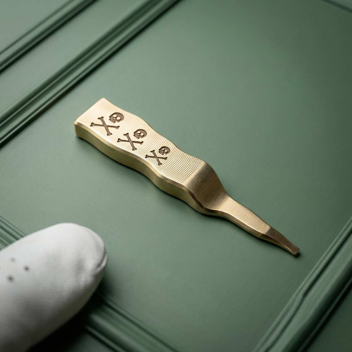 This is a brass Condent pennant pitch tool featuring three skull and crossbones on the front.