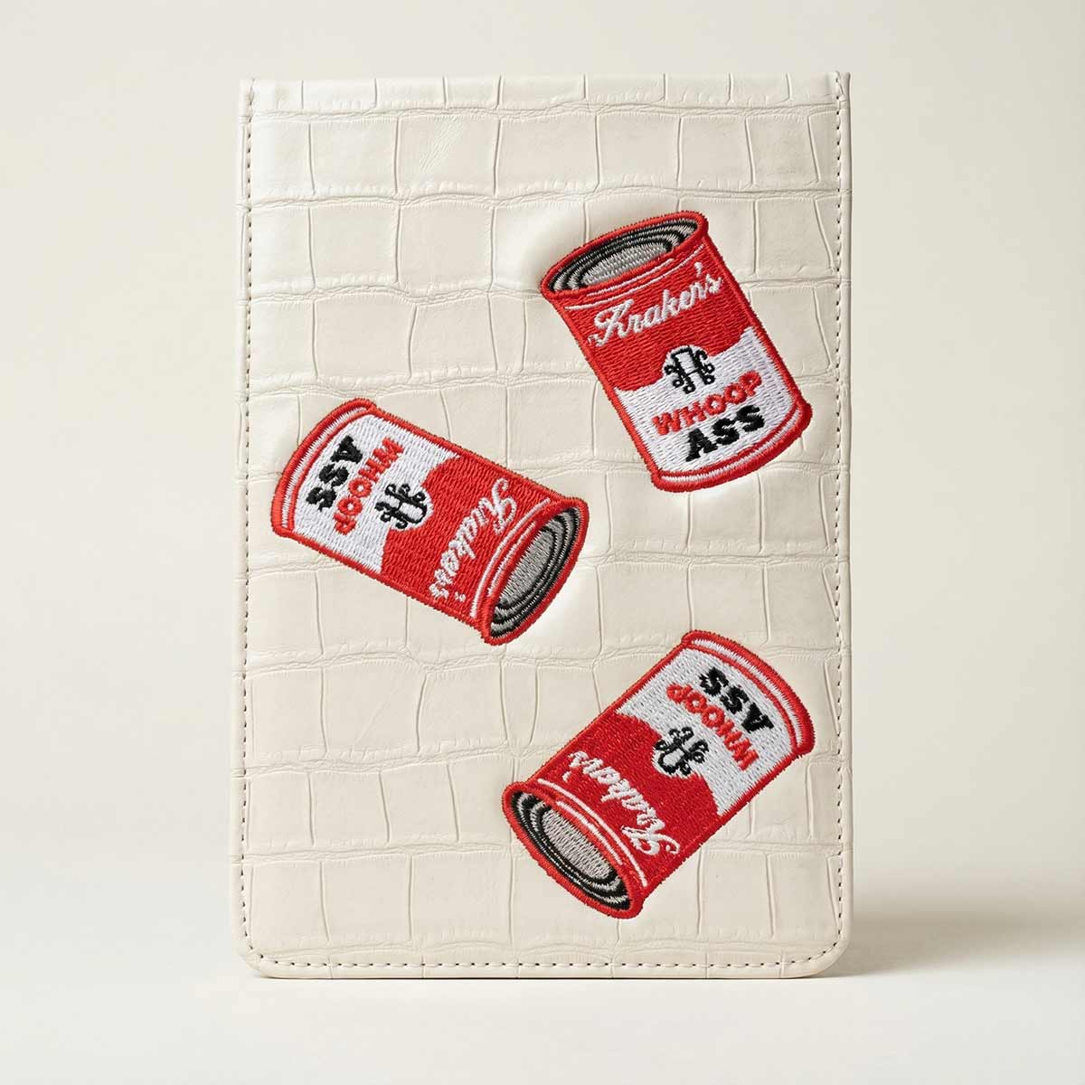 Golf Yardage Book with three red and white kraken can of whoop ass embroidery cans on a textured beige background