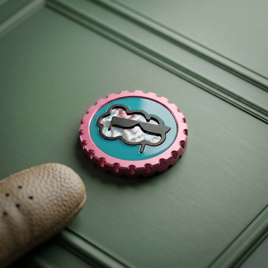 Cloud Nine golf ball marker front view — teal epoxy inlay with 3D-printed black border and hand-finished stainless steel perlage cloud motif, anodized pink aluminum body, serrated edge