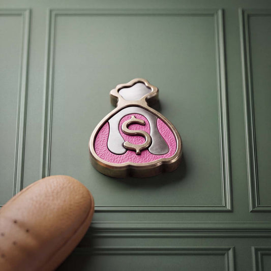 Front of Kraken Golf Compound ball marker, a machined brass money bag with a raised dollar sign over hot-pink drip and stainless steel inlays