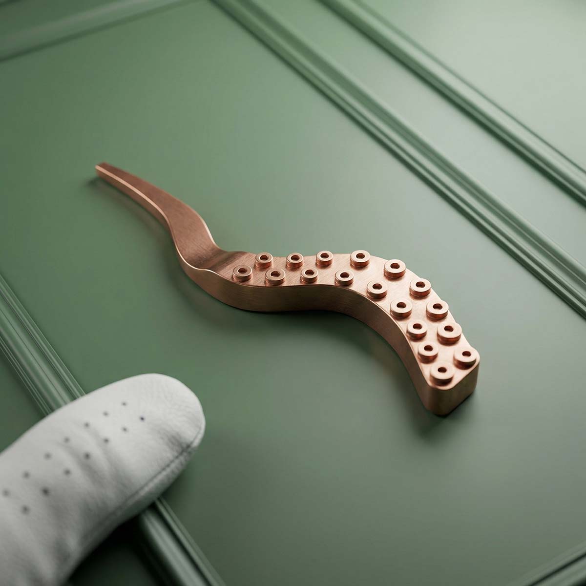 Copper pitch tool on green background shaped like an octopus tentacle.