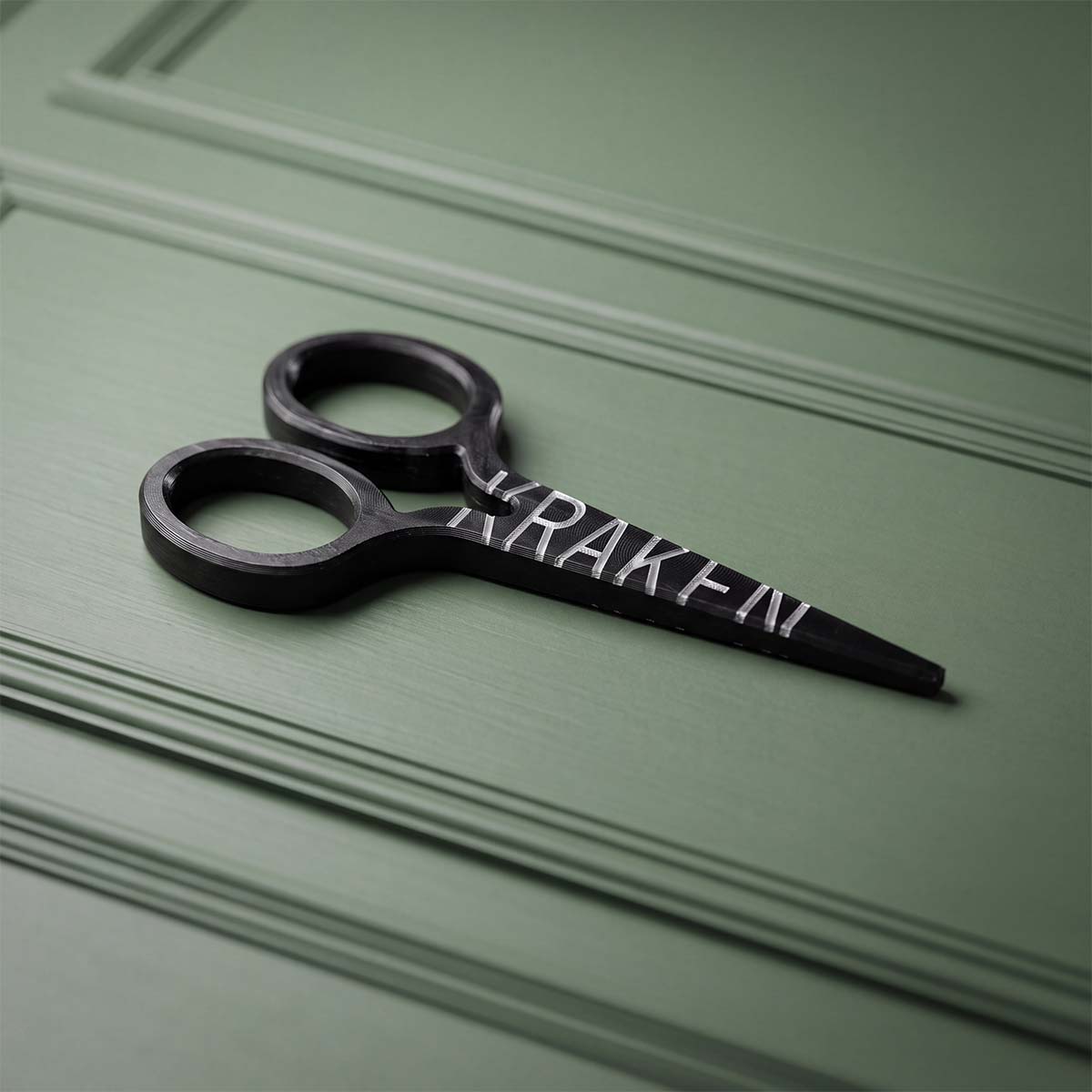 Back of the CUT LINE scissor divot tool with KRAKEN wordmark laser-marked through black oxide to bare carbon steel