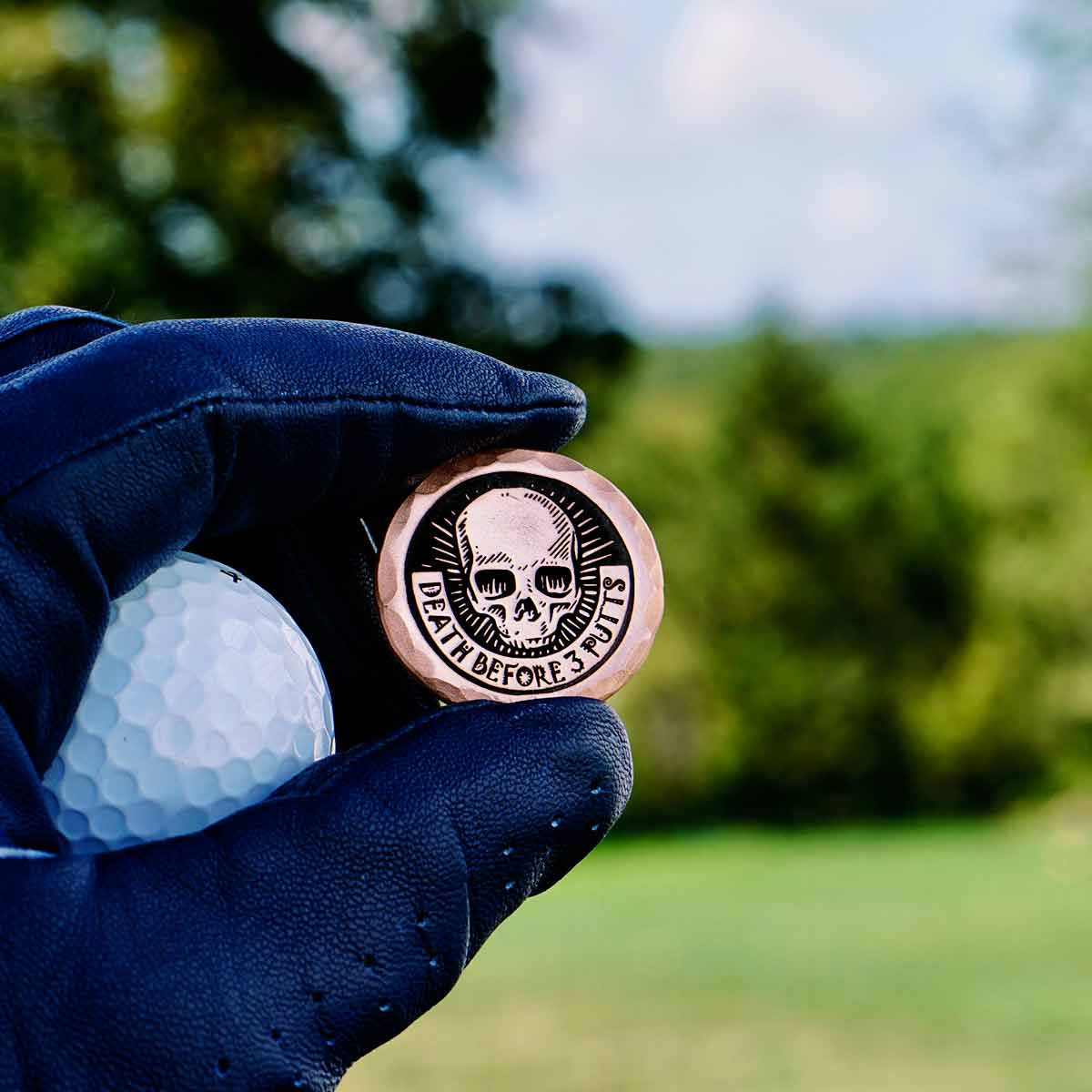Death Before 3 Putts Golf Ball Marker in Copper on the golf course being held by a navy blue golf glove