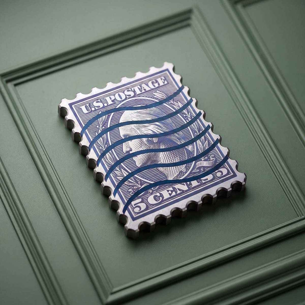 FACE VALUE golf ball marker in blue anodized titanium, shaped like a vintage five-cent postage stamp 