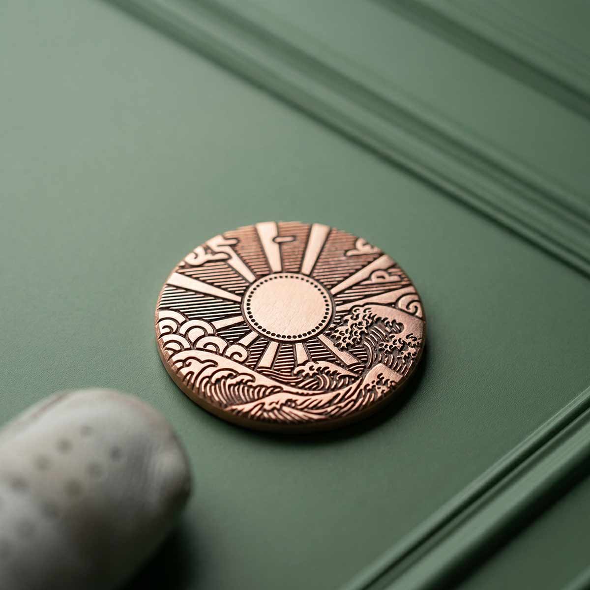 Hinode copper golf ball marker on green background
