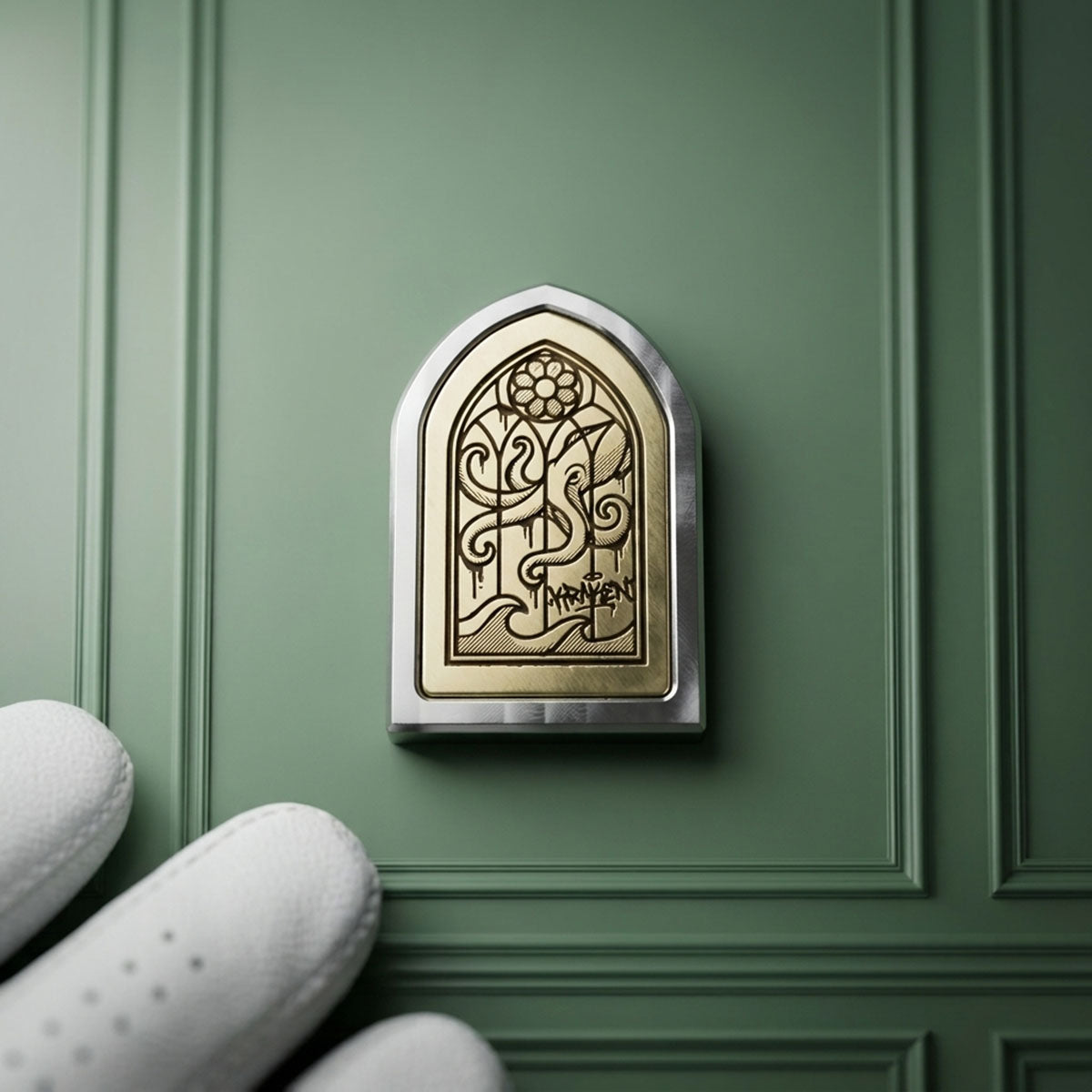 Kraken Golf HOLY WATER ball marker in 303 stainless steel with laser-engraved brass gothic window inlay, held against a green wall