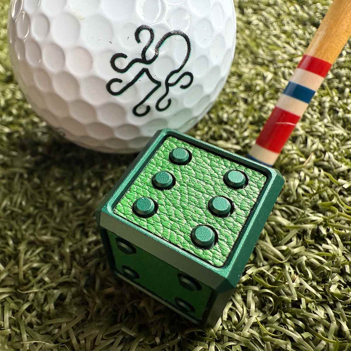 A bold, cube-shaped golf ball marker with green anodized finish and leather inlay - a high-end tool for players who flex on the green.