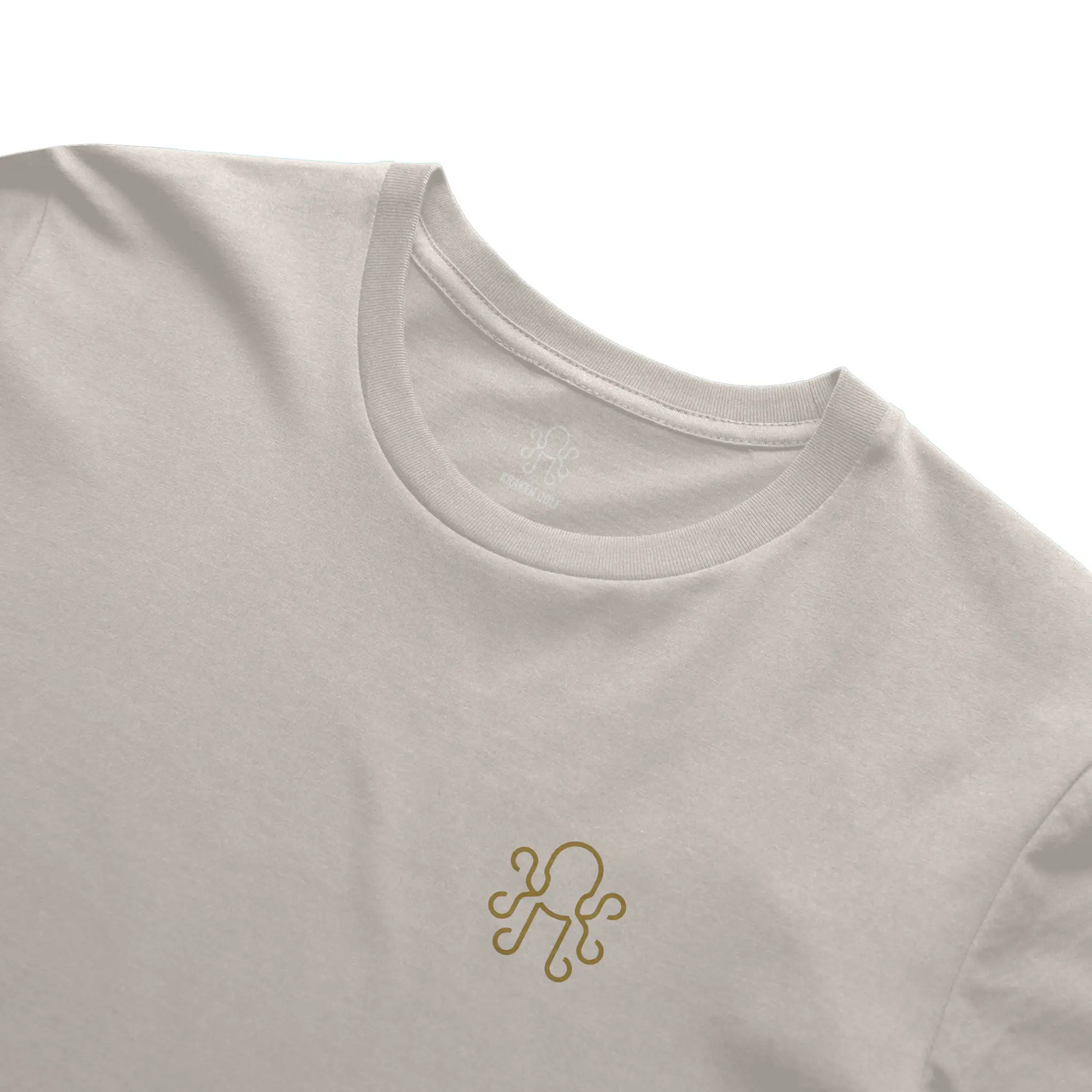 Close-up of brass Kraken crest on ivory heavyweight t-shirt (left chest)