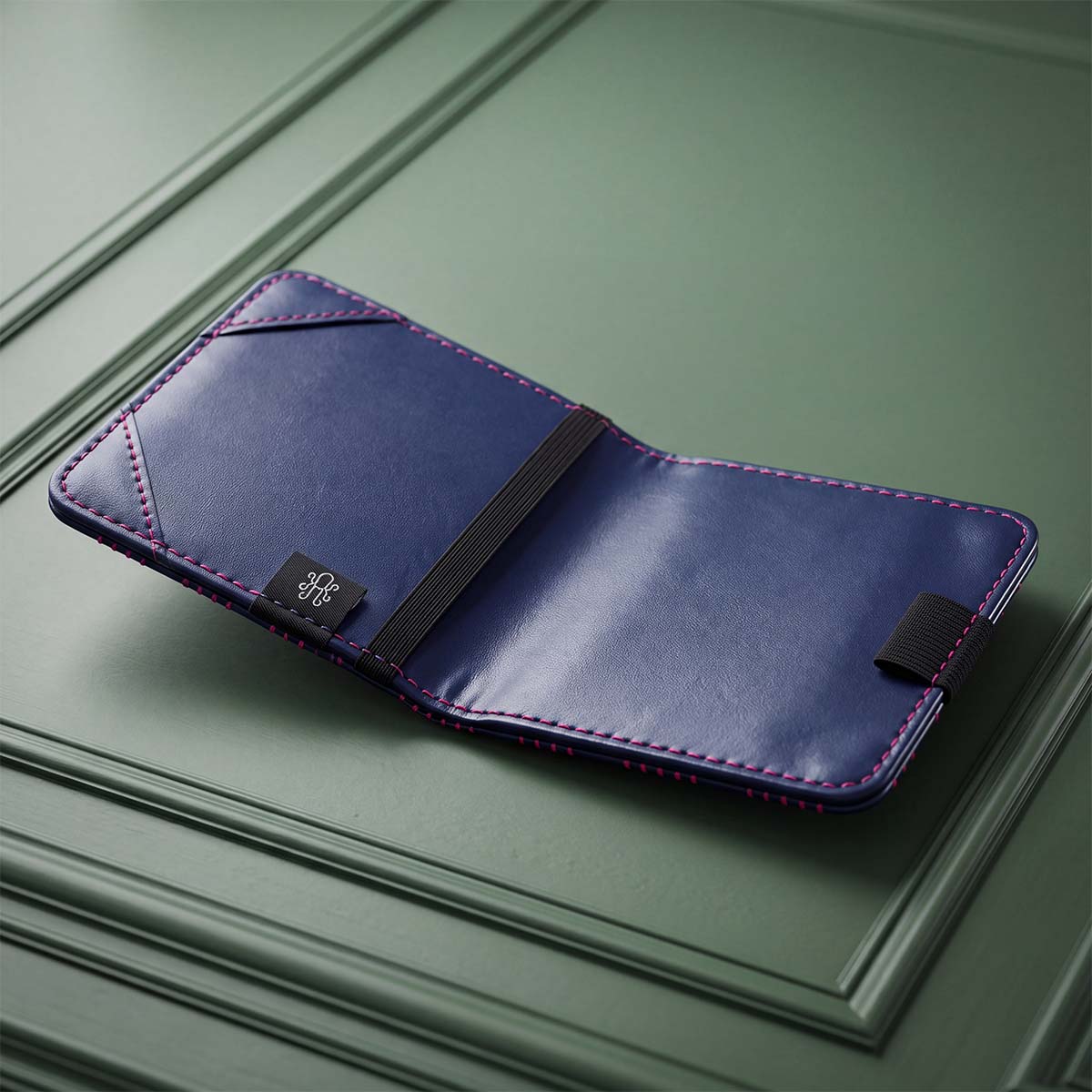 Open navy yardage book holder showing pebble-grain interior with pink contrast stitching, elastic band, and corner slots