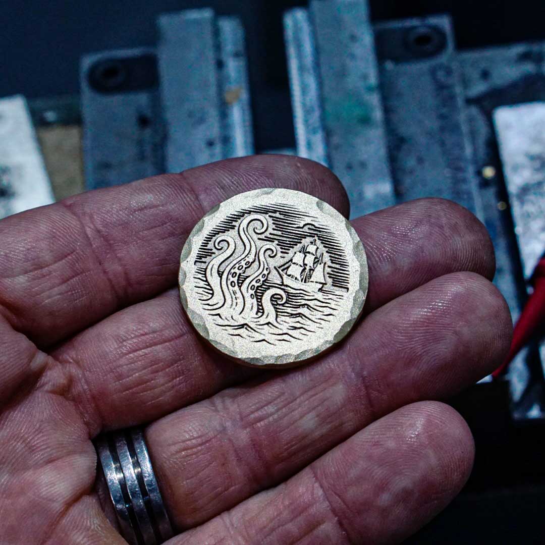 Brass golf ball marker with Kraken tentacles emerging from ocean and ship in background