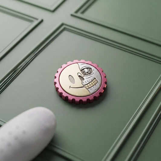 Kraken Golf Last Laugh ball marker with brass smiley and stainless steel skull inlay on a pink anodized aluminum body, gear-tooth EDC edge, resting on a green surface
