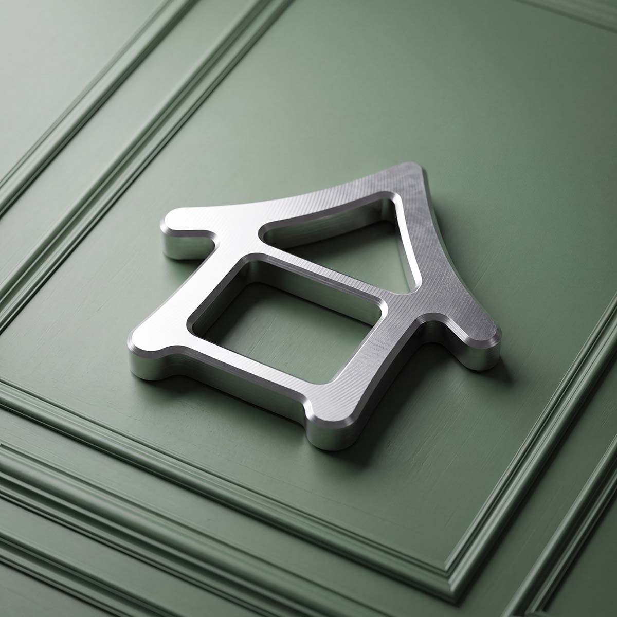 Kraken Golf Machiya stainless steel golf ball marker, house-shaped open frame with visible mill marks, on sage green panel