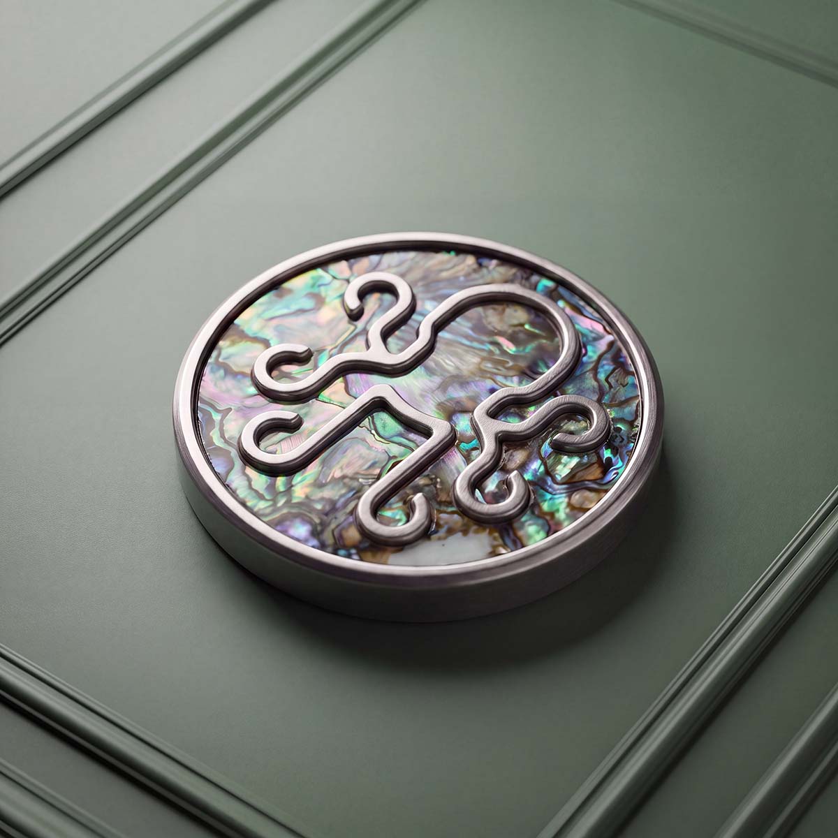 NACRE golf ball marker with iridescent abalone shell inlay and raised stainless steel Kraken logo