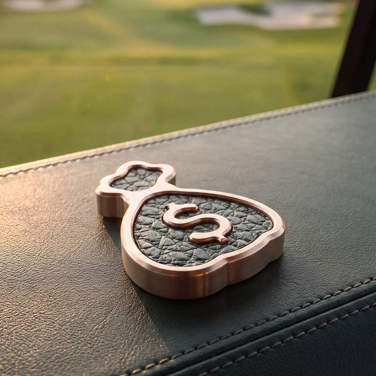 Nassau brass money bag golf ball marker with green Dollaro leather inlay on a golf cart seat overlooking the course at sunset