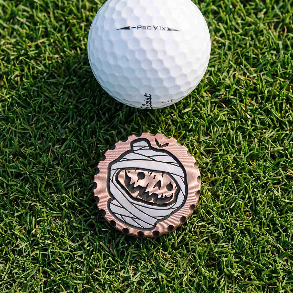HOLLOWED copper Halloween golf ball marker resting on putting green