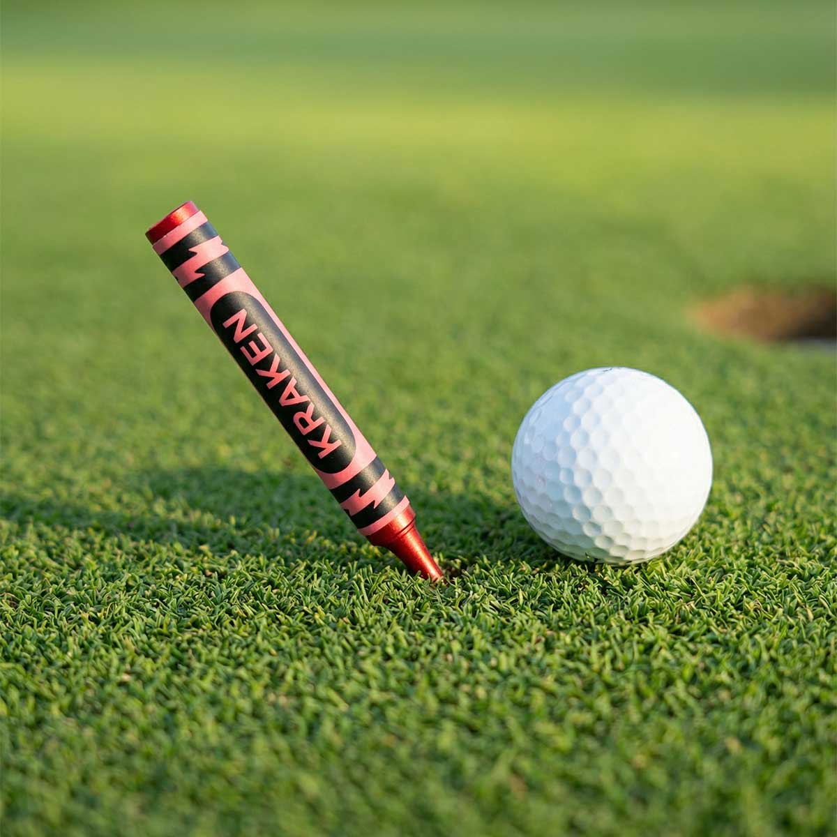 Red Birdie Crayon Divot Tool in red anodized aluminum, shown on putting green
