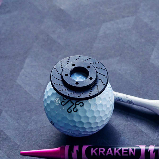 Golf ball with a Kraken Black Rotor Ball Marker on a textured gray surface