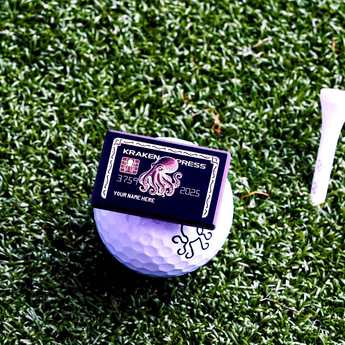 Titanium ball marker styled like a black credit card with Kraken design