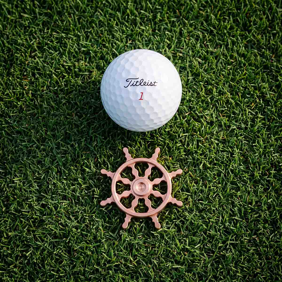 The Helm copper ship wheel golf ball marker beside a golf ball on a putting green