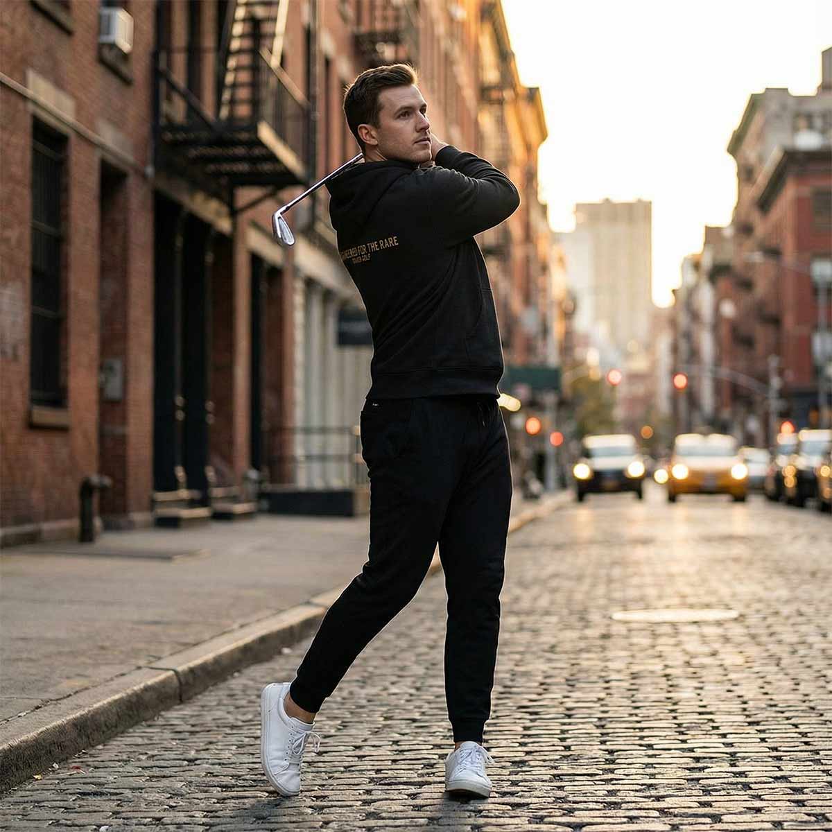 Golfer Craig wearing the Rare Hoodie holding a golf club on a city street.
