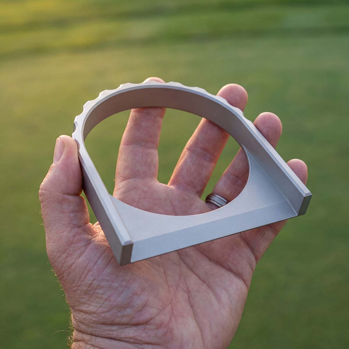 The Vision stainless steel putting portal held in hand showing sculptural cathedral arch silhouette and scalloped crown detail
