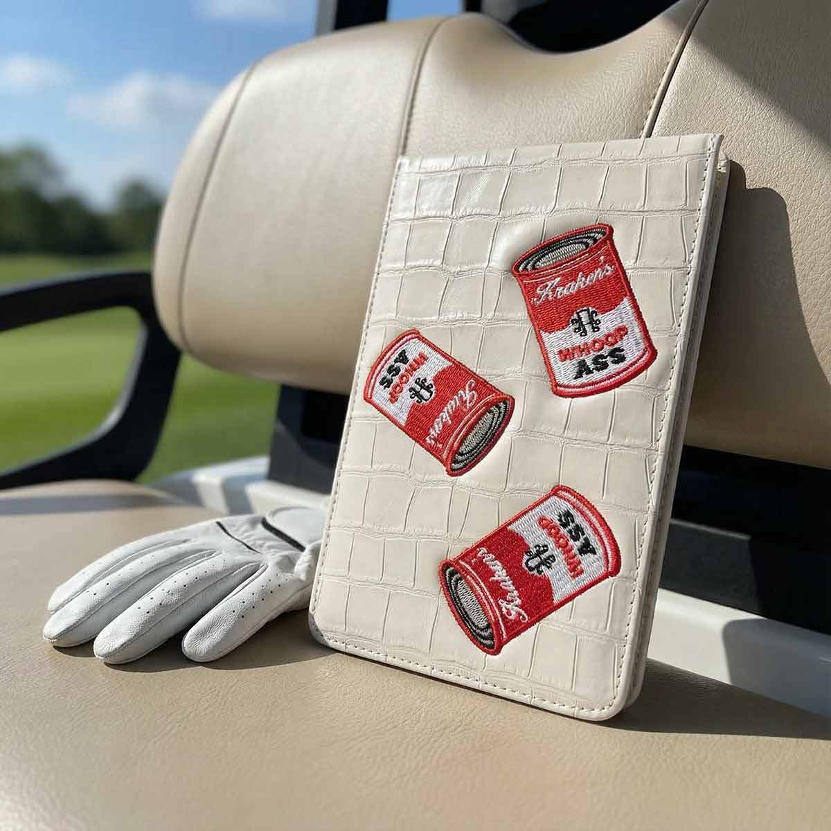 White crocodile-textured yardage book with red patches on a golf cart seat